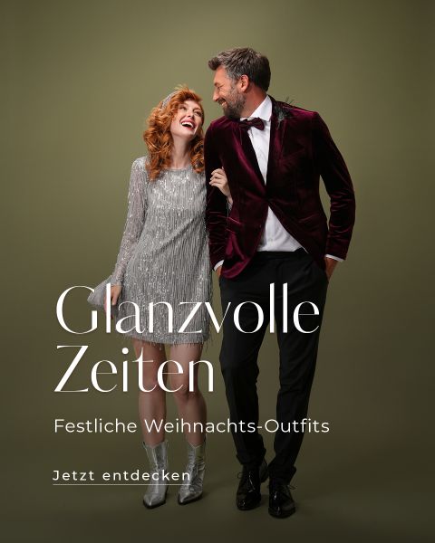 Eine Frau in einem silbernen Fransenkleid und ein Mann in einer Samtjacke teilen einen freudigen Moment vor grünem Hintergrund. Weißer Text lautet: „Glanzvolle Zeiten – Festliche Weihnachts-Outfits. Jetzt entdecken.“