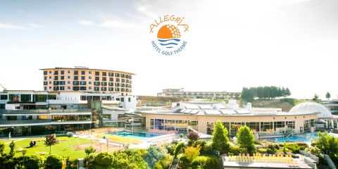 Eine malerische Aussicht auf das Alegria Hotel Golf Theme mit modernen Gebäuden, die von üppigem Grün umgeben sind. Es gibt Außenpools mit Sonnenliegen und ein Logo mit dem Text „Alegria Hotel Golf Theme“ oben im Bild.