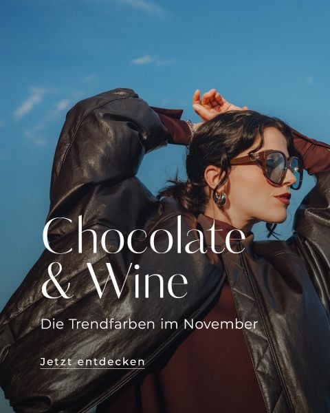 Eine Frau in einer braunen Lederjacke und mit Sonnenbrille posiert vor einem blauen Himmel. Der Text lautet: "Chocolate & Wine - Die Trendfarben im November. Jetzt entdecken.