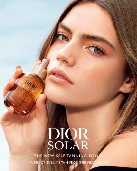 Eine Frau mit strahlender Haut hält ein Fläschchen mit Bräunungstropfen von Dior Solar in der Nähe ihres Gesichts, auf dem in weißer Schrift der Produktname und der Slogan zu lesen sind.