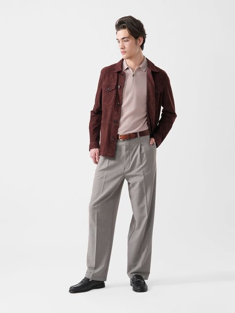 Mann mit weinroter Jacke, beigem Polohemd, grauer Hose und schwarzen Schuhen, der vor einem schlichten weißen Hintergrund steht und zur Seite schaut.