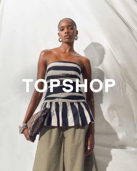 Eine Frau in einem trägerlosen gestreiften Oberteil und einer khakifarbenen Hose posiert vor einem weißen Hintergrund und hält eine Clutch. Das Wort "TOPSHOP" erscheint über dem Bild.
