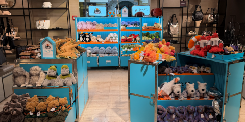 Turquoise display units in a toy shop filled with colorful stuffed animals, plush bears, and accessories on shelves and tables inside."