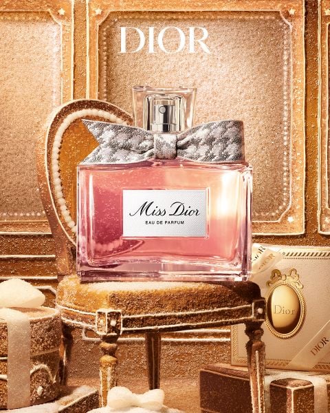 Ein Flakon „Miss Dior Eau de Parfum“ mit einer gemusterten Schleife, der in der Mitte eines kleinen, verzierten Hockers steht, der von Geschenkboxen umgeben ist.