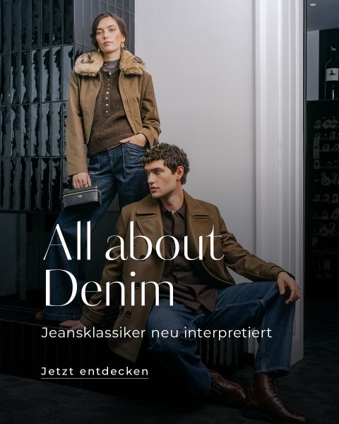 Zwei Models in braunen Jacken und Jeans posieren in einem Innenraum neben einer schwarzen Treppe. Der Text lautet: „Alles rund um Denim. Jeansklassiker neu interpretiert. Jetzt entdecken.“.