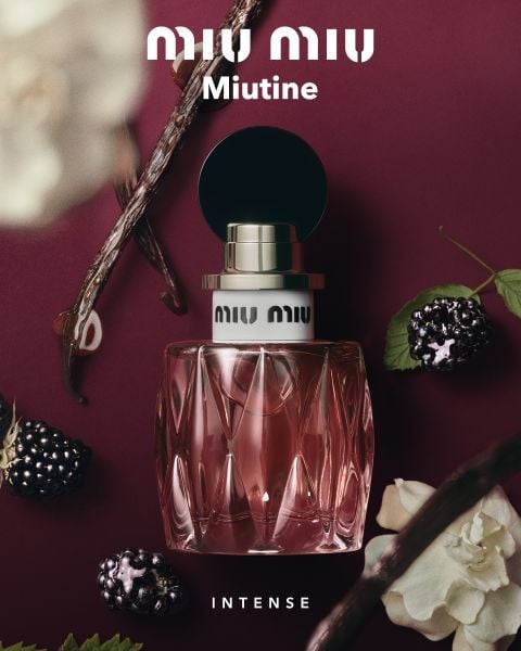 Ein rosa Parfümflakon mit der Aufschrift „Miu Miu Miutine“ auf burgunderrotem Hintergrund, umgeben von Beeren, Vanilleschoten und weißen Blüten.