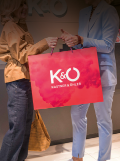 Zwei Frauen halten eine rote K&O Kastner & Öhler-Einkaufstasche in der Hand.